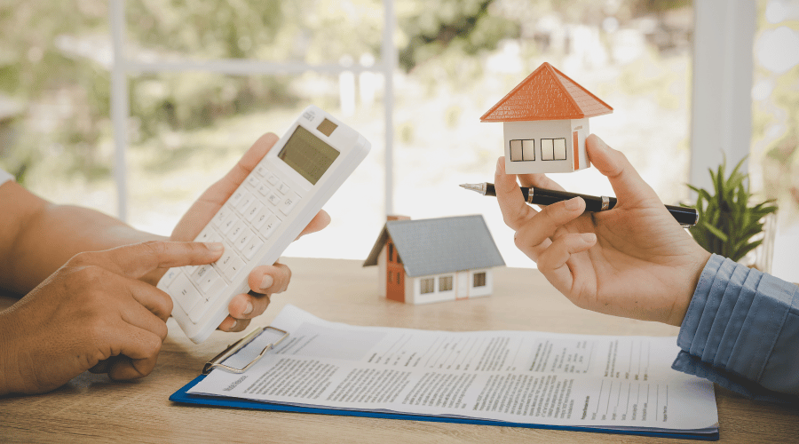Hand holds a model house above paperwork and a calculator